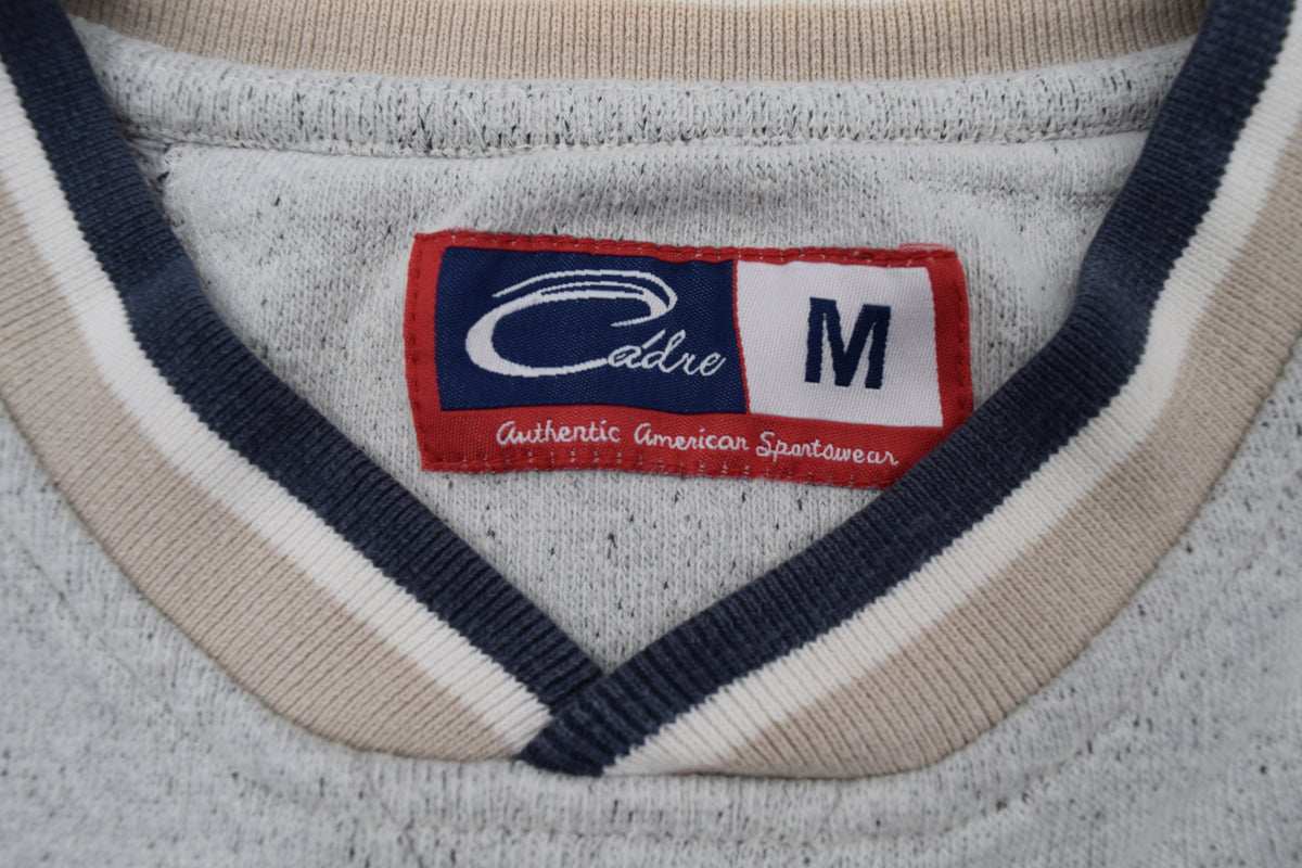 Close-up of a University of Michigan crewneck sweatshirt collar with a V-neck trim in heather gray, navy blue, and cream, featuring a red and white Cadre brand label.