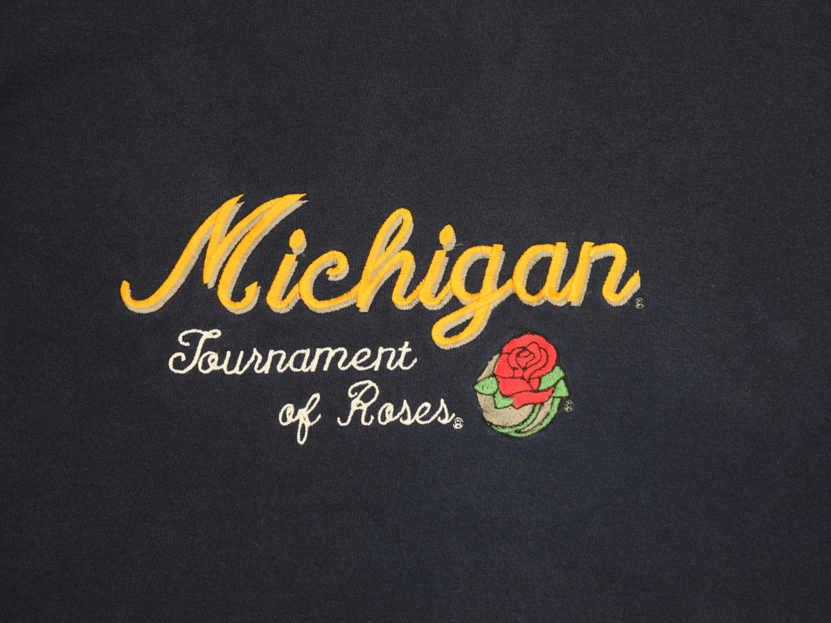 Close-up of University of Michigan navy blue crewneck sweatshirt embroidered text reading 'Michigan Tournament of Roses' in yellow and white, plus a small red rose graphic.