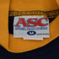 Close-up of the inside collar of a University of Michigan crewneck sweatshirt showing a white sewn-in label for ASC Apparel Sales Company with red and blue lettering, set against a yellow ribbed collar and navy blue knit fabric.
