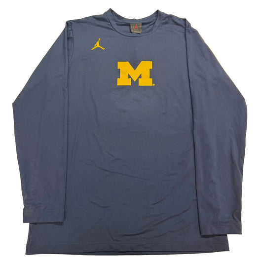 Blue long-sleeve shirt with yellow 'M' logo on a beige background